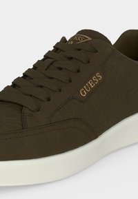 Baskets Guess marron en tissu texturé, lacets à l'avant, logo doré sur le côté et semelle en caoutchouc blanche.