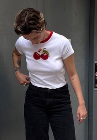 Balta trumpa rankovėmis marškinėliai su raudona apykakle, priekyje dekoruoti išsiuvinėtomis raudonomis vyšniomis ir žaliu lapu, derinami su juodomis džinsinėmis kelnėmis.