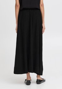 Jupe maxi noire avec une taille élastique, fabriquée en tissu doux, offrant une coupe décontractée et des fentes latérales pour plus de confort.