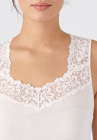 Tank top blanco con un delicado borde de encaje alrededor del escote. La textura es suave y lisa, con un diseño de escote bajo.