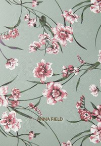 Gėlių audinys su rožinėmis ir baltomis gėlėmis bei žaliais lapais šviesiai žaliame tekstūruotame fone; „ANNA FIELD“ auksinėmis raidėmis.