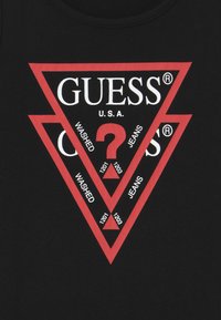 Czarny t-shirt z centralnym czerwonym logo w kształcie trójkąta z napisem "GUESS U.S.A." oraz różnymi odniesieniami do "WASHED" i "JEANS."