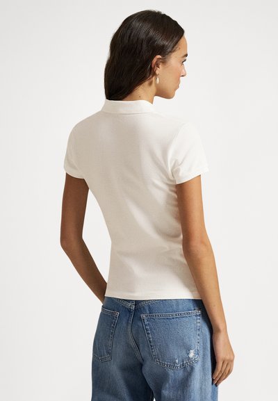 Polo branca de manga curta, com gola e corte ajustado, combinada com jeans de ganga azul clara desgastados.