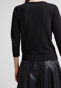 Czarny sweter dziany z rękawami o długości trzech czwartych, z teksturowanymi bocznymi panelami i ściągaczem u dołu, zestawiony z plisowaną czarną skórzaną spódnicą.