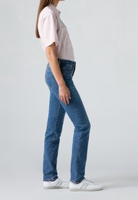 Chemise rayée rose à manches courtes, jean bleu et baskets blanches. Accent sur une coupe décontractée et des couleurs contrastées. Design minimaliste.