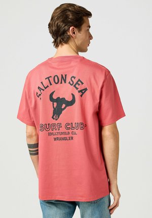 Rotes Baumwoll-T-Shirt mit einem schwarzen Bullenkopf-Design und dem Text "SALTON SEA SURF CLUB" auf dem Rücken. Klassischer Rundhalsausschnitt.