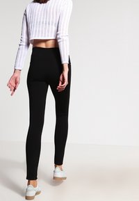 Leggings noirs avec une coupe ajustée, une texture lisse et une taille mi-haute, associés à un haut court blanc côtelé et des baskets légères.