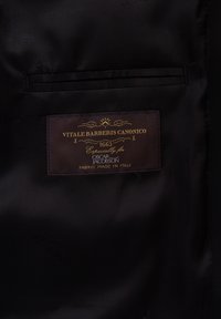 Zwarte stof met een gladde textuur heeft een bruine label met de tekst "Vitale Barberis Canonico 1663, speciaal voor Oscar Jacobson, stof gemaakt in Italië."