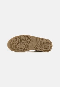 Semelle extérieure de sneaker Nike en caoutchouc marron. Présente un motif circulaire avec des nervures pour l'adhérence. Surface texturée avec détail du logo.