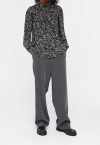 Blouse à motifs noir et blanc avec col mandarin, coupe décontractée, associée à un pantalon gris ample et des chaussures noires à semelles épaisses.