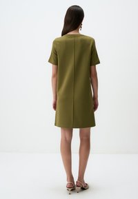 Kurzärmliges olivgrünes Kleid mit geradem Schnitt und Rückennahtdetails, aus einem glatten Stoff gefertigt. Tragen mit minimalistischen Absatzsandalen.