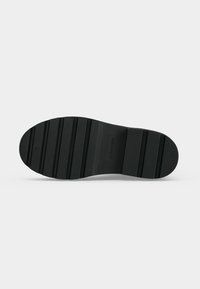 Semelle de chaussure noire avec des rainures horizontales et le logo Calvin Klein au centre sur fond blanc.