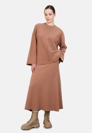 Brown, oversized sweater with long sleeves and side seam detail, paired with a matching long skirt. Worn with beige lace-up combat boots.