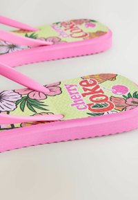 Poros rožinių šlepečių su žaliais padais, ant kurių pavaizduoti gėlių raštai ir užrašas „cherry love“, padėtos ant šviesaus paviršiaus.