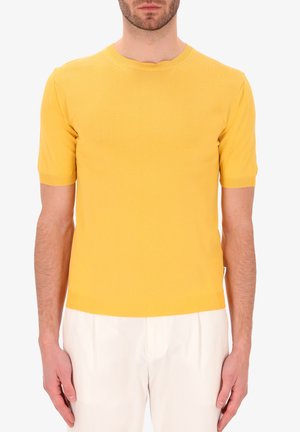 Top a maniche corte giallo realizzato in maglia, caratterizzato da un collo rotondo e polsini a coste, realizzato in materiale morbido, abbinato a pantaloni di colore chiaro.