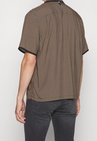 Korte mouwen shirt met een geometrisch patroon in bruin en beige, met een zwarte kraag en accenten. Soepele stof en comfortabele pasvorm.