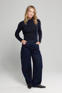 Top a maniche lunghe a costine blu navy abbinato a jeans in denim scuri a vita alta e a gamba larga. Modella in piedi con le mani sui fianchi, indossa scarpe nere.