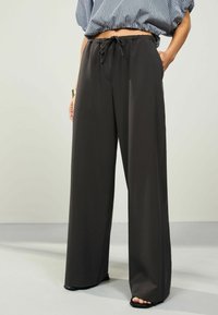 Pantaloni a gamba larga in grigio scuro, realizzati in un tessuto liscio. Presentano una vita elastica con coulisse e un design minimalista.