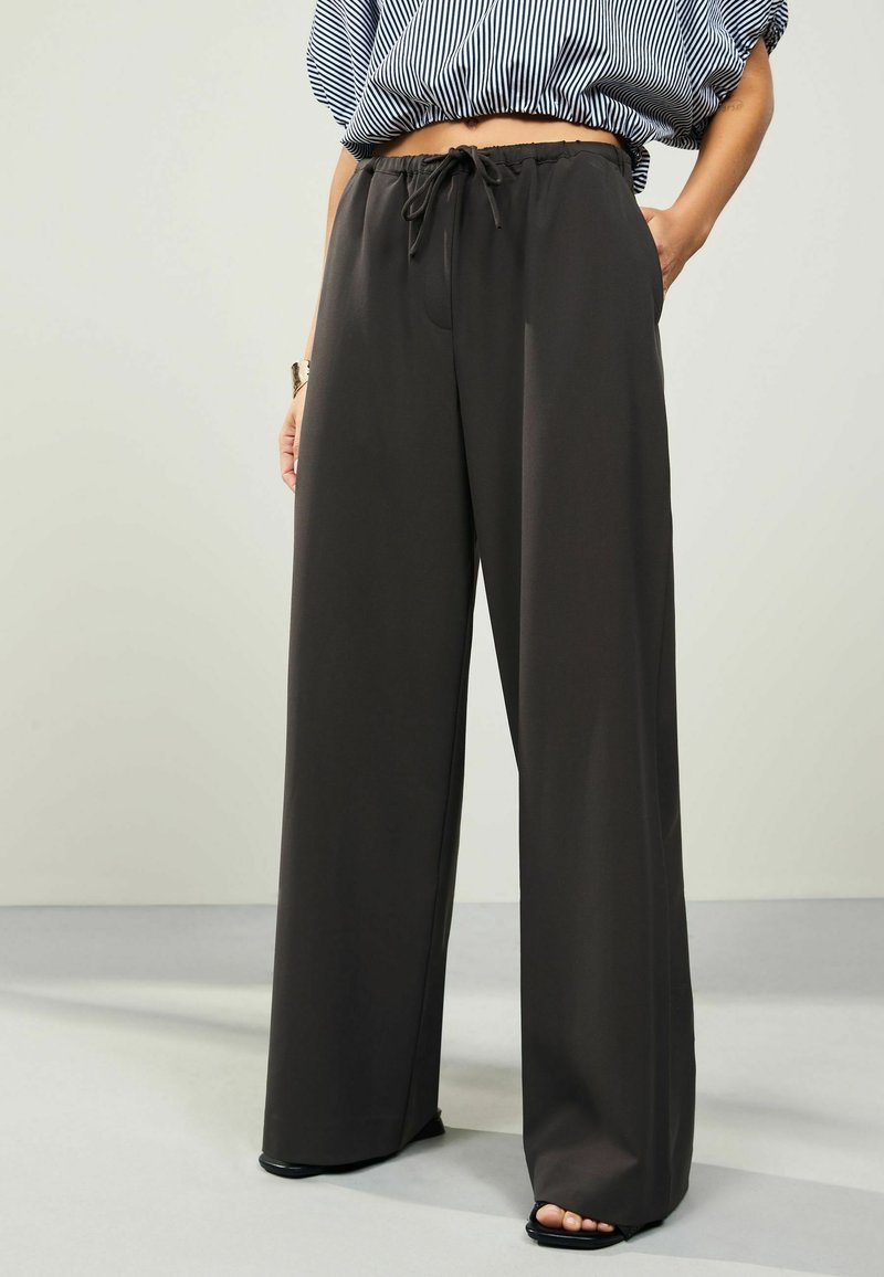 Pantaloni a gamba larga in grigio scuro, realizzati in un tessuto liscio. Presentano una vita elastica con coulisse e un design minimalista.