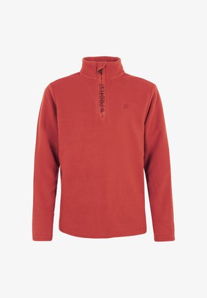 Garçon souriant aux cheveux bouclés portant une polaire rouge avec fermeture éclair quart de zip, un pantalon vert d'extérieur et des chaussures noires, debout sur un fond blanc.
