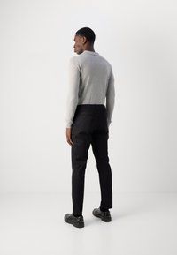 Chemise à manches longues gris clair associée à un pantalon noir slim et des chaussures noires, avec un col côtelé et une texture lisse.