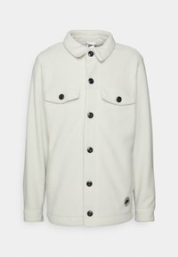 Vit fleecejacka med krage, svarta knappar, två bröstfickor och en rund logotyp. Mjuk textur och avslappnad passform.