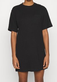 Robe T-shirt noire en tissu doux, avec des manches courtes, un col rond et une petite poche poitrine. Design simple et ample.
