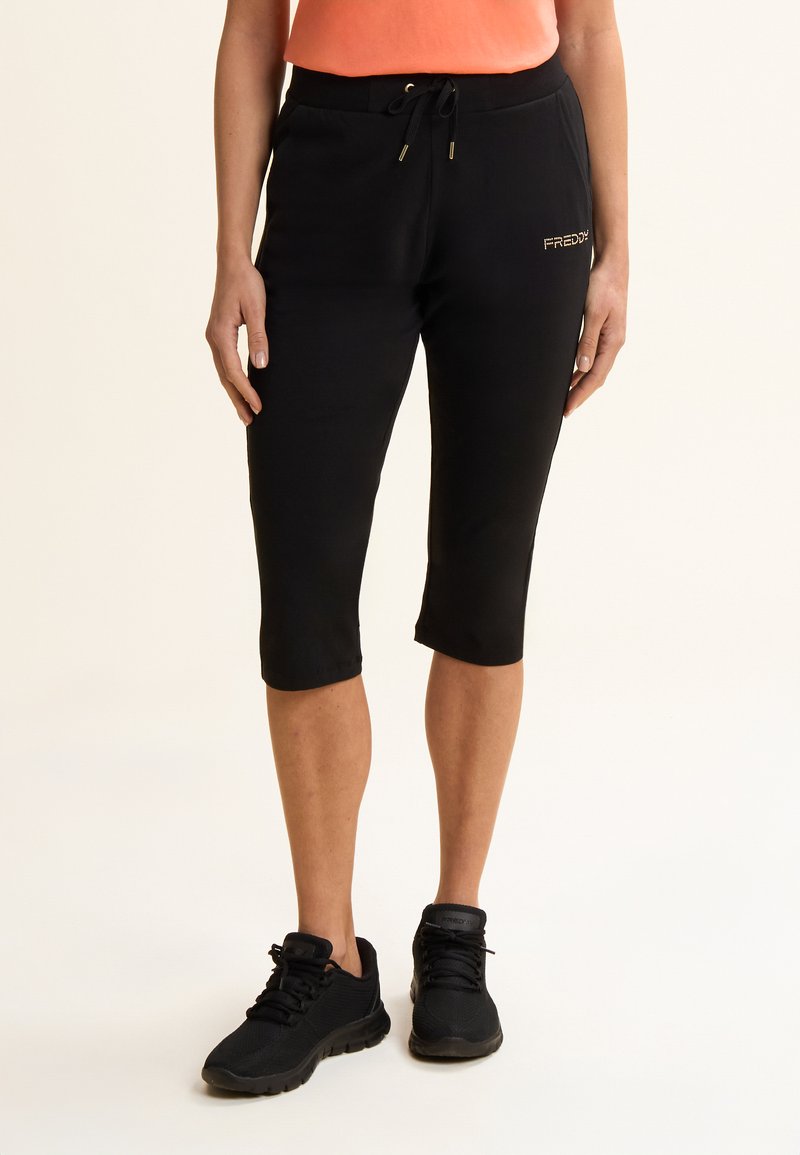 Pantalones deportivos negros recortados con cintura elástica y cordón ajustable. Presentan un logotipo dorado "FREDDY" en el lateral y una textura lisa.