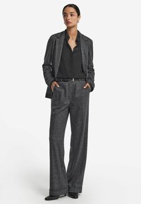 Grå kavaj i sillbensmönster kombinerad med en svart blus och vida byxor. Outfiten har en figursydd silhuett och stilrena svarta ankelboots.