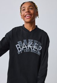 Sort langærmet T-shirt med V-udskæring, der har et flerfarvet grafisk tryk af "BAKER" og "by TED BAKER" i forskellige skrifttyper.