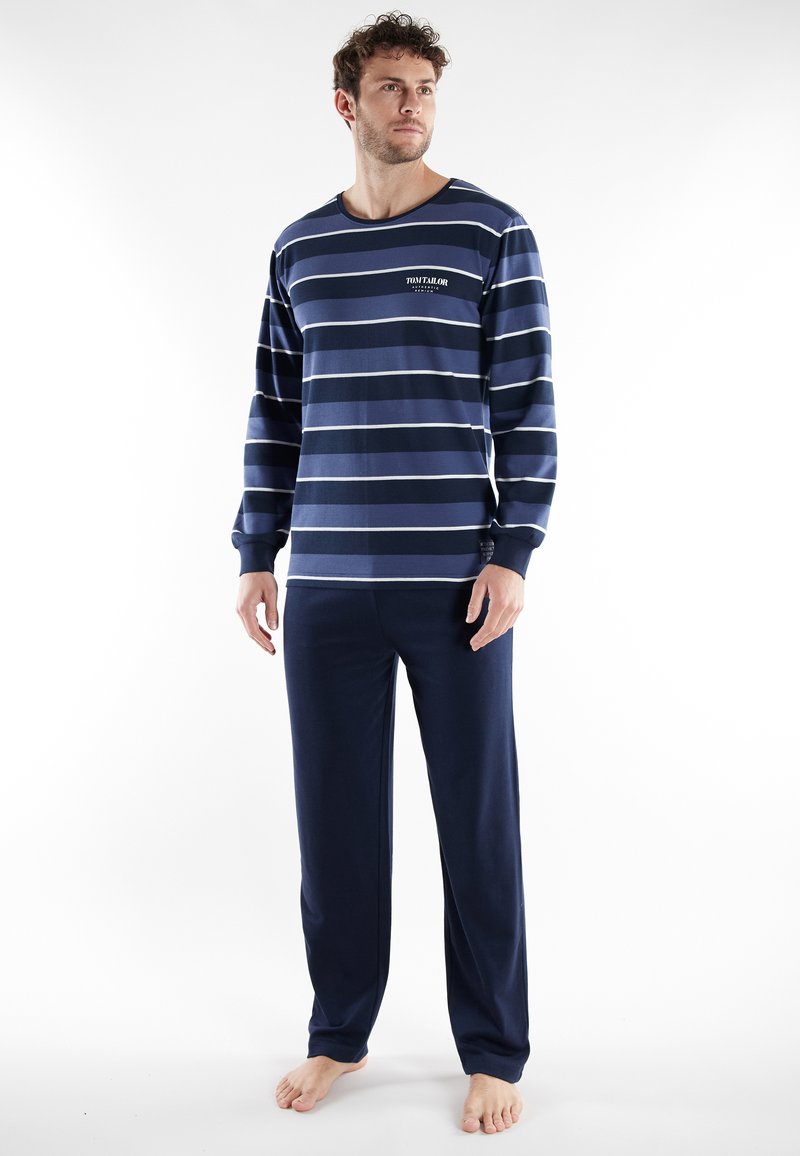 Ensemble de pyjama bleu marine avec manches longues et pantalon, arborant des rayures blanches horizontales et un petit logo sur la poitrine. Tissu au toucher doux.