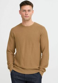 Suéter de punto texturizado en marrón con cuello redondo y mangas largas, con puños y bajo acanalados. Combinado con pantalones de mezclilla oscuros.
