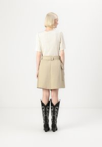 Gonna beige chiaro con cintura in vita e tasche, abbinata a un top crema texturizzato e stivali western neri ricamati.