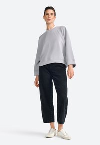 Sudadera de gran tamaño en gris claro con mangas anchas, combinada con jeans negros ajustados y zapatillas blancas. Diseño sencillo, estilo casual.