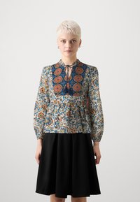 Květinová blůza s dlouhými rukávy, s modro-oranžovým vzorem, šněrovacím výstřihem a siluetou peplum, kombinovaná s černou sukní.