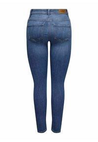 Kitsad sinised teksad, millel on kulunud pesu, viis taskut ja pruun nahktembeldus tagumise vöökoha peal. Sile denimi tekstuur.