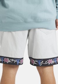 Person wearing white shorts with black floral and blue bull skull pattern trim, paired with a light blue sweatshirt.