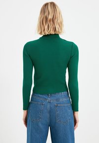 Grünes geripptes Langarmoberteil mit hohem Kragen, kombiniert mit blauen hochsitztenden Jeans mit Gesäßtaschen und geradem Schnitt.