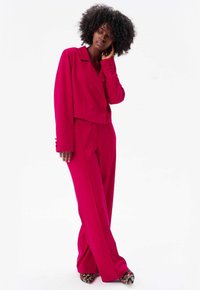 Fuchsia op maat gemaakt pak met een dubbelgeknoopte cropped blazer en een broek met wijde pijpen. Heeft een gladde stof en hooggehakte schoenen met een bloemenpatroon.