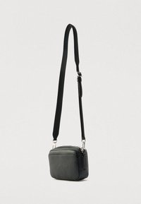 Čierna kožená taška cez rameno s obdĺžnikovým tvarom, zapínaním na zips, nastaviteľným remienkom a striebornými kovovými doplnkami. Hladká textúra, minimalistický dizajn.