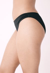 Čierny bikiny spodok s hladkou textúrou, nízkym strihom a zahnutými švíkmi pozdĺž okrajov, ktorý predvádza minimalistický štýl.