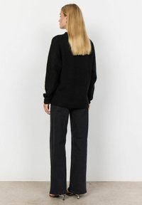 Pulover negru, supradimensionat, cu mâneci lungi, dintr-un material texturat. Asortat cu pantaloni negri cu talie înaltă și pantofi cu toc cu imprimeu animal.
