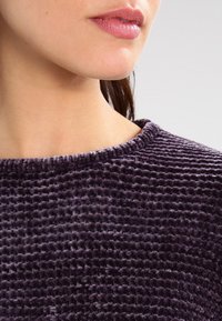 Tejido texturizado morado con un patrón acanalado, que presenta un escote redondeado y un acabado suave. Vista en primer plano que muestra el detalle en el diseño del material.