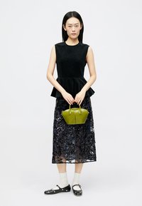 Top peplum texturat negru, suprapus peste o fustă lungă, cu paiete negre. Modelul ține o geantă mică verde, purtând șosete albe și pantofi negri.