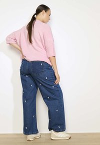 Rozā adīta džemperis, brīva piegriezuma. Tumši zilas platās bikses ar nelielu baltu ziedu izšuvumu. Beigās kurpes ar vieglu zoli. Visā tekstūrā ir gluda.