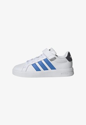 Scarpa da ginnastica bianca con strisce blu, chiusura con lacci e cinturino in velcro, linguetta del tallone con marchio e suola piatta.