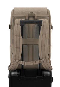 Beige rugzak met gevoerde bandjes bevestigd aan een zwarte koffer met wieltjes en een uitgeschoven handvat voor reisgemak.