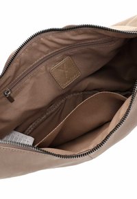 Interno della borsa tan con rivestimento in morbido tessuto, dotato di una tasca con zip e una texture liscia. Include una piccola etichetta in pelle con logo.