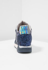 Sneaker blu navy con tacco glitterato, linguetta posteriore olografica iridescente, suola scura e testo del marchio "Replay", mostrato da dietro su sfondo bianco.