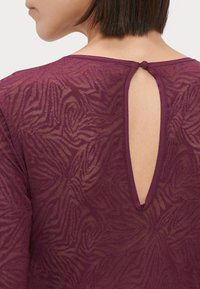 Lila hálós felső levélmintás textúrával, hátul kulcslyuknyílással és gombos zárással, hosszú ujjakkal.